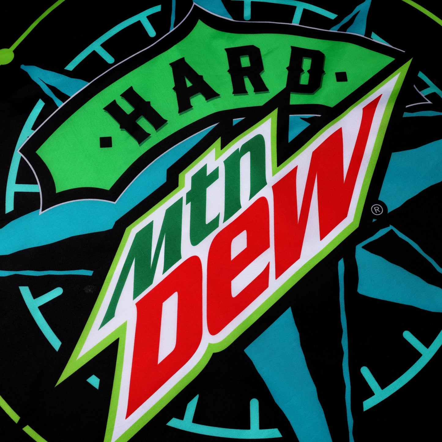 Close-up of the Hard MTN DEW flag showcasing the central logo with "HARD" in green above the slanted "MTN DEW" in green with a red outline and red lettering, all overlaid on a teal and neon green compass design against a black background.