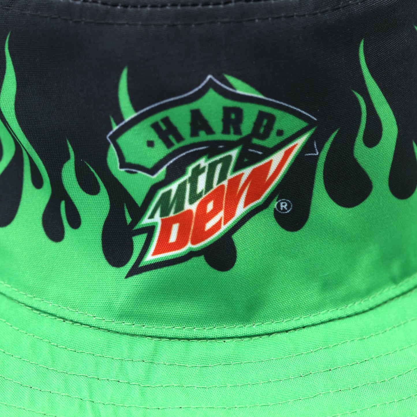 Close-up of the Hard Mountain Dew logo on the side of the bucket hat with green flame patterns. The logo is clearly visible against the flame design.
