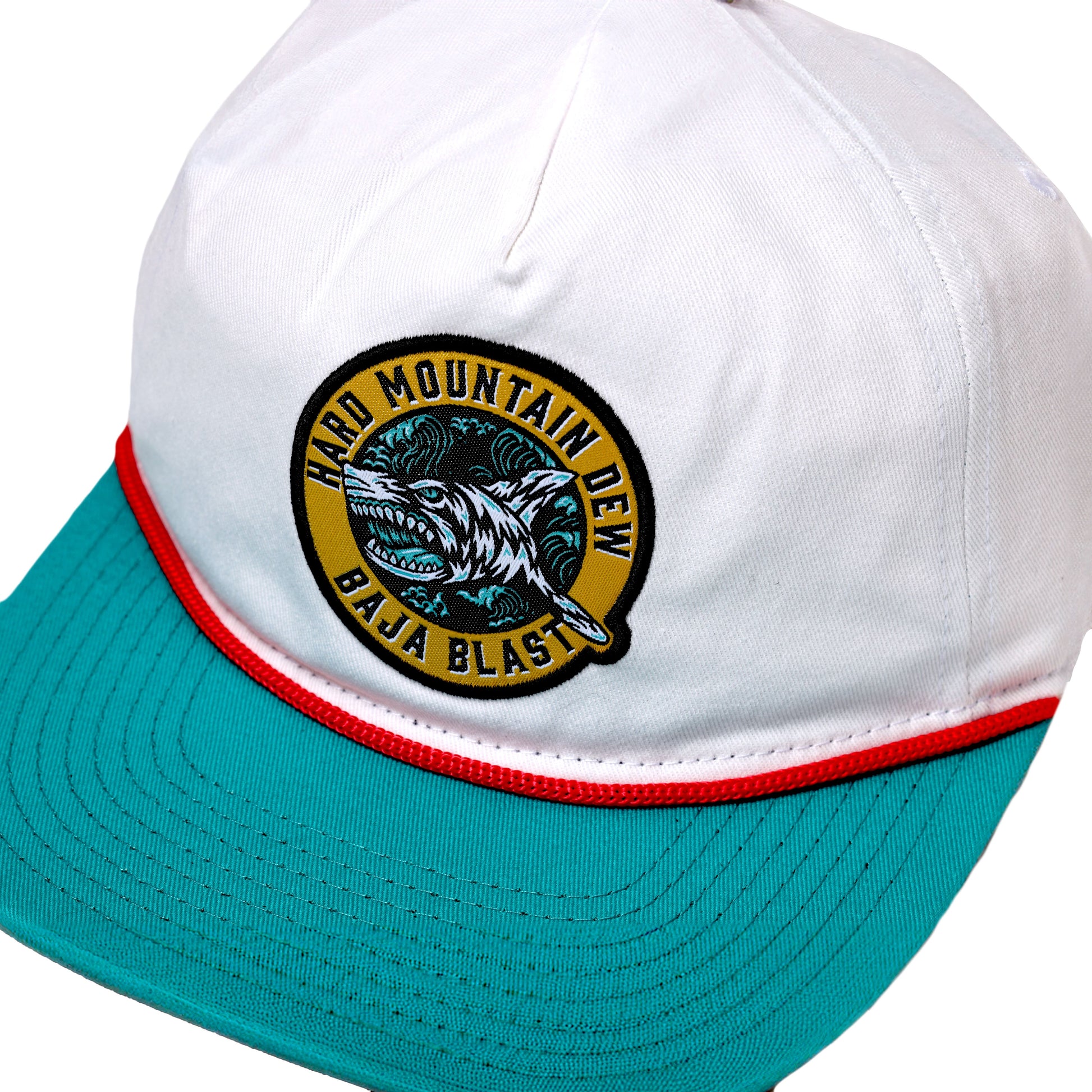 White hat with red lining between teal brim. Hat has a yellow emblem with writing "Hard Mountain Dew Baja Blast" and shark in the center.