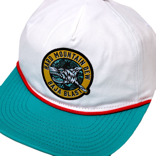 White hat with red lining between teal brim. Hat has a yellow emblem with writing "Hard Mountain Dew Baja Blast" and shark in the center.