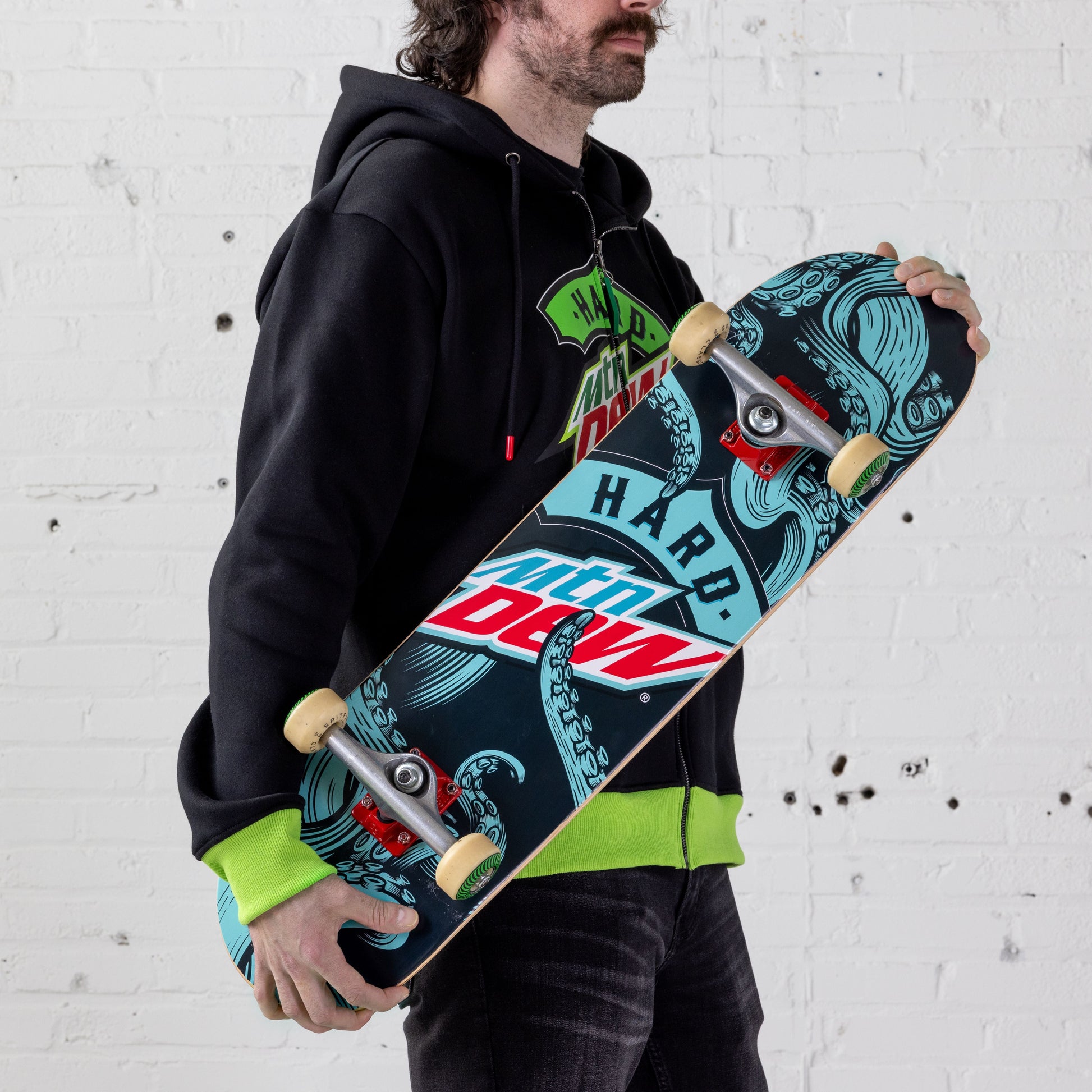 Model holding a skate deck with a teal, black, and red Hard Mountain Dew logo, surrounded by teal octopus tentacle arms