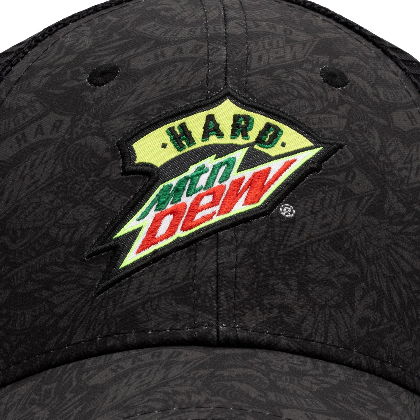 Close-up of the embroidered patch on the trucker hat. The Hard Mountain Dew logo is prominently featured, stitched with precision over the tonal logo pattern on the front of the hat.