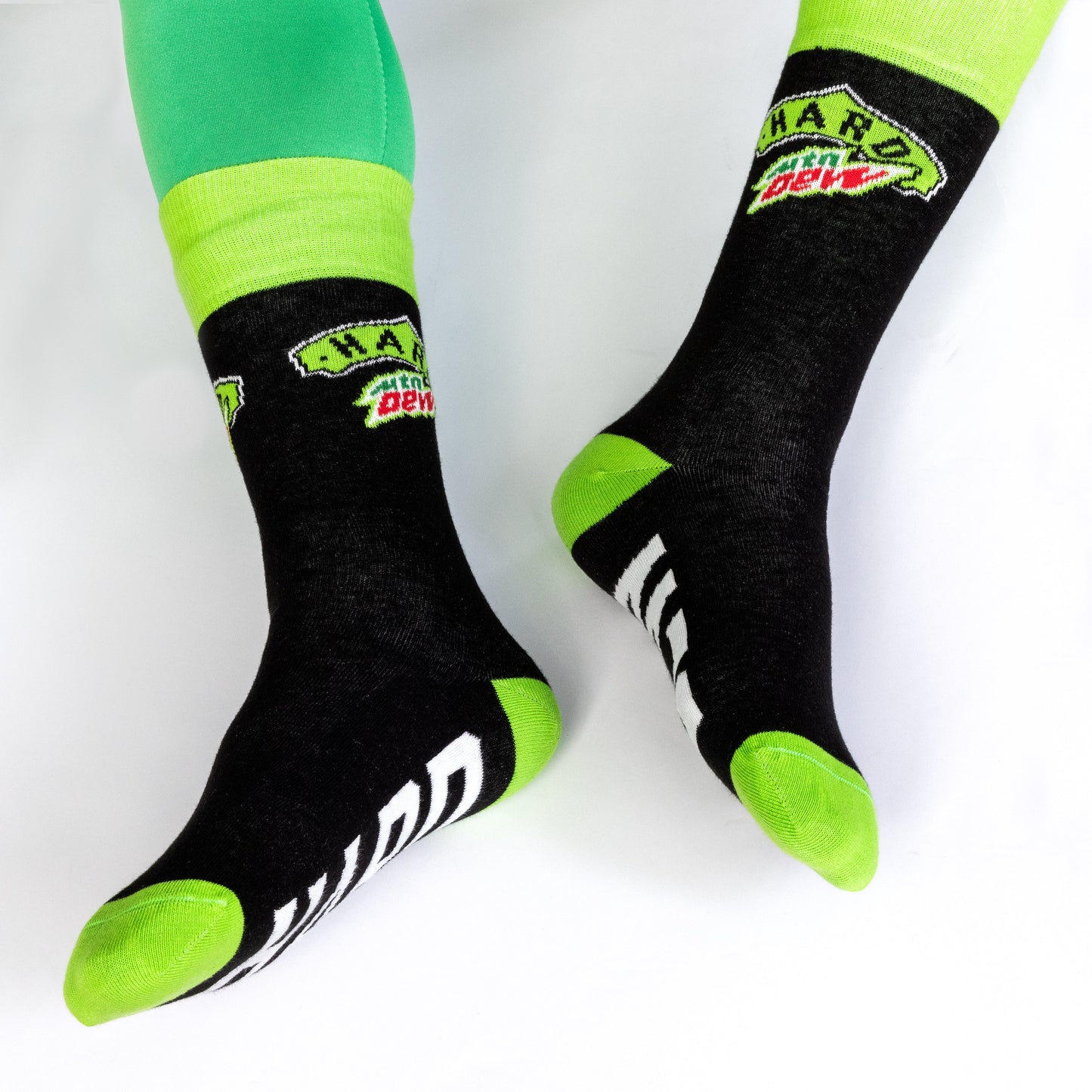 Socks featured on a model to show mid-calf length. The socks are mostly black with bright green details on the cuff, heel, and toe, and the Hard Mountain Dew logo is visible on the ankle portion.