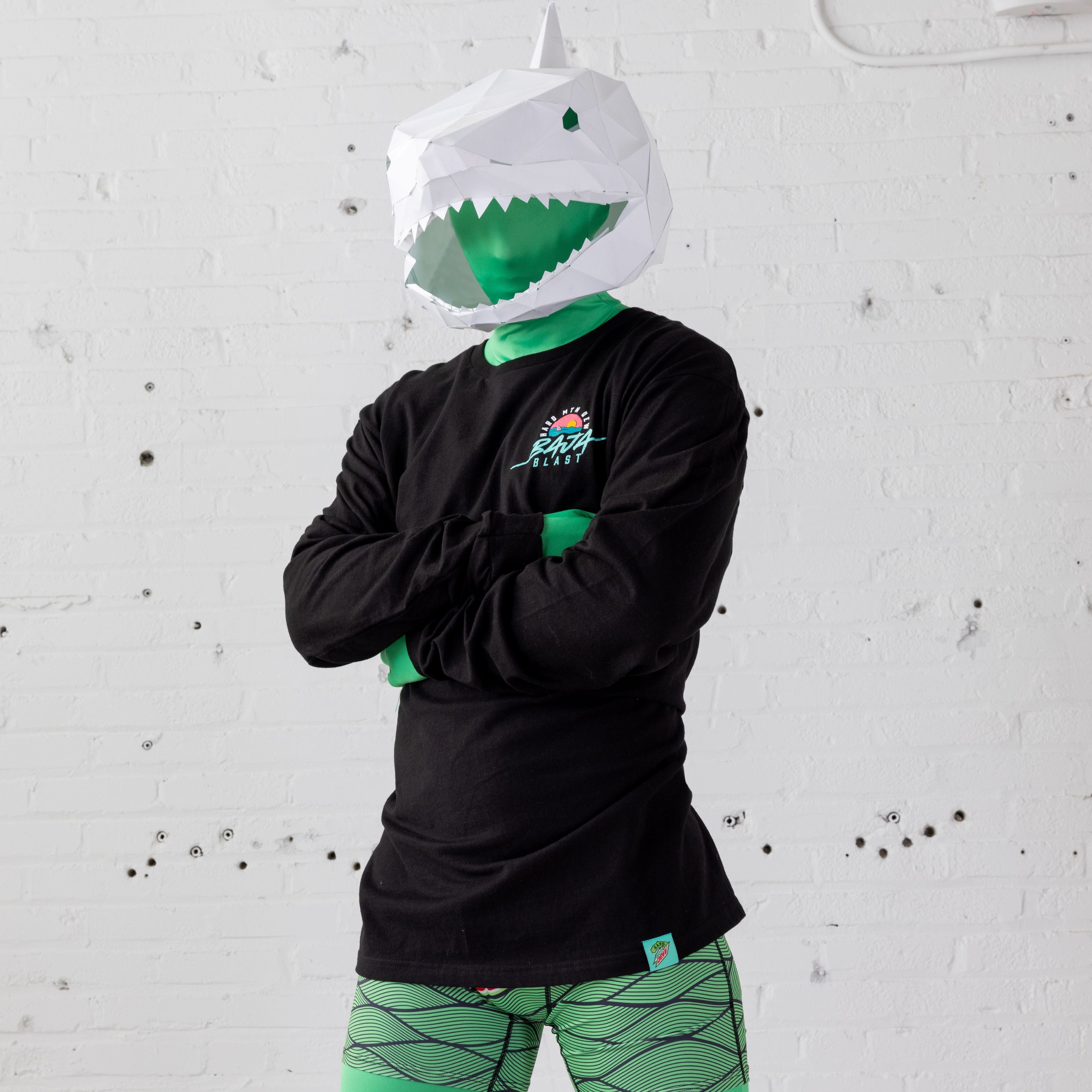 Model wearing a black Baja Blast t-shirt over a full-body green skin suit and a shark mascot-style headpiece. The t-shirt features retro 90s artwork on the left chest, and the model’s costume complements the shark theme.